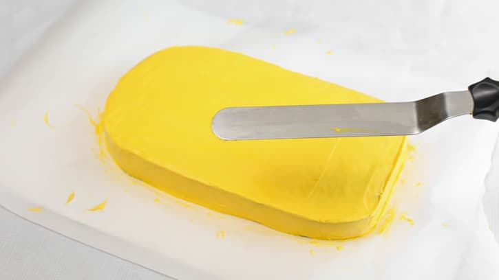 smoothing out yellow frosting on sheet cake