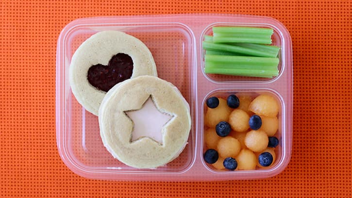 pancake sandwiches in compartmented lunch container with fruit and celery