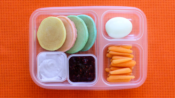 compartmented lunch container with pancakes and dipping sauces, an egg and carrots
