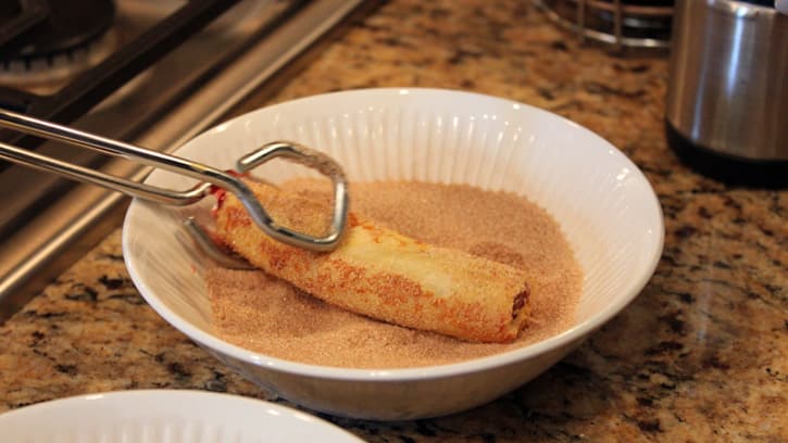 dipping cooked roll up in cinnamon sugar mixture