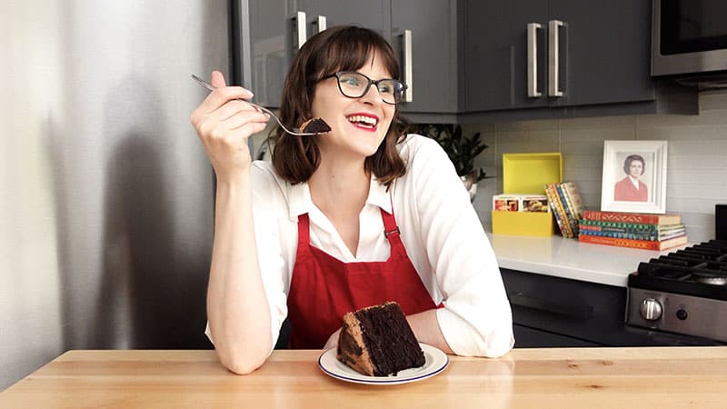 Melinda Sekela in her kitchen with a piece of chocolate cake.
