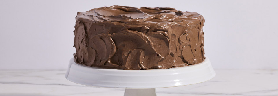 Four-layer chocolate cake covered in creamy chocolate frosting with a large slice removed and plated in front of the cake.