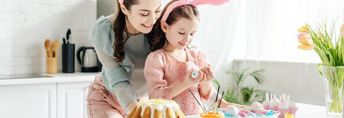 Mom and daughter wearing bunny ears, in the kitchen, decorating Easter eggs