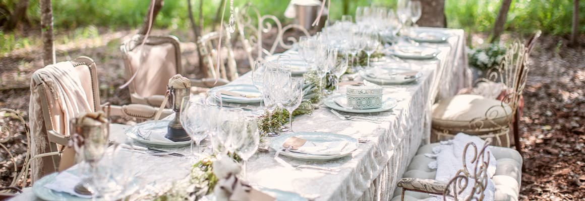 Table and chairs in an outdoor setting. Table is set with white linen, china, wine glasses and flowers.