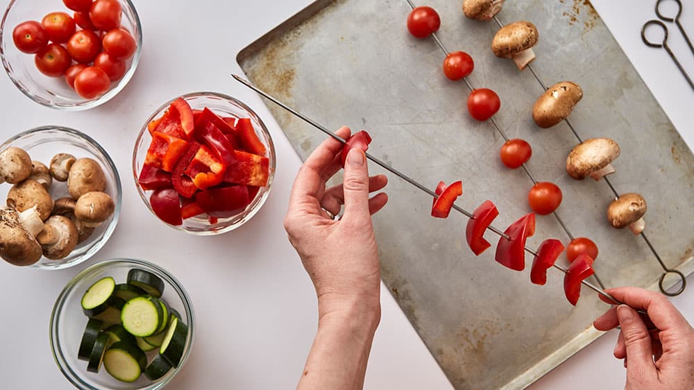 Threading red pepper pieces onto skewers to make vegetable kabobs
