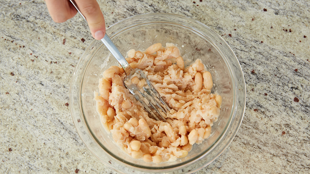 In small bowl, add beans, and lightly mash with potato masher or fork. 