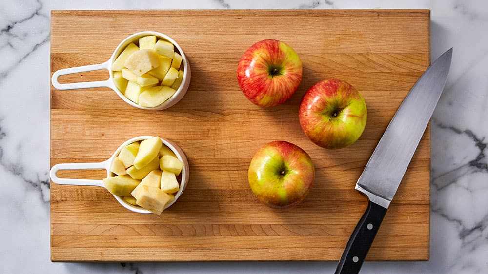 2 cups of apples chopped next to 3 medium-sized apples on a cutting board 