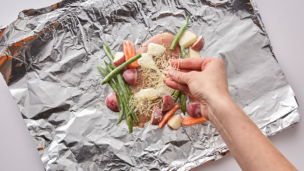 Adding vegetables to chicken in foil packs