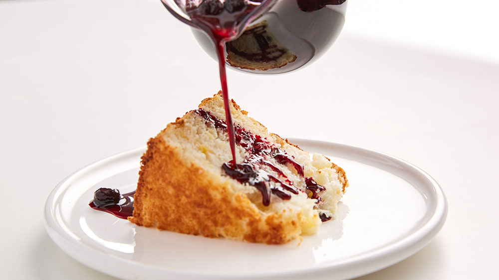 Pouring blueberry sauce over angel food cake