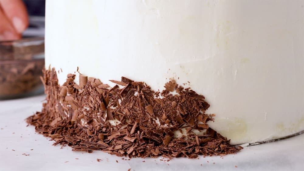 adding chocolate shavings to frosted cake