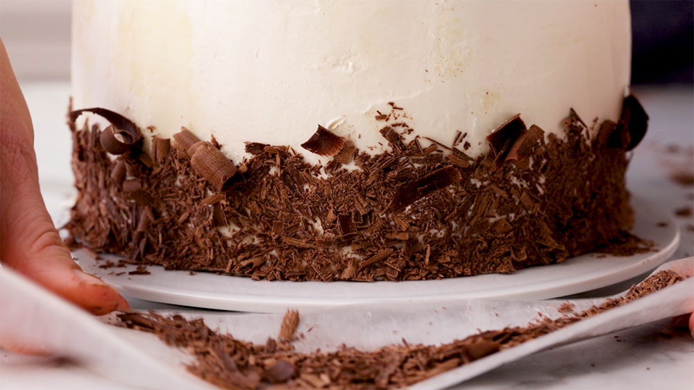 adding chocolate shavings to frosted cake
