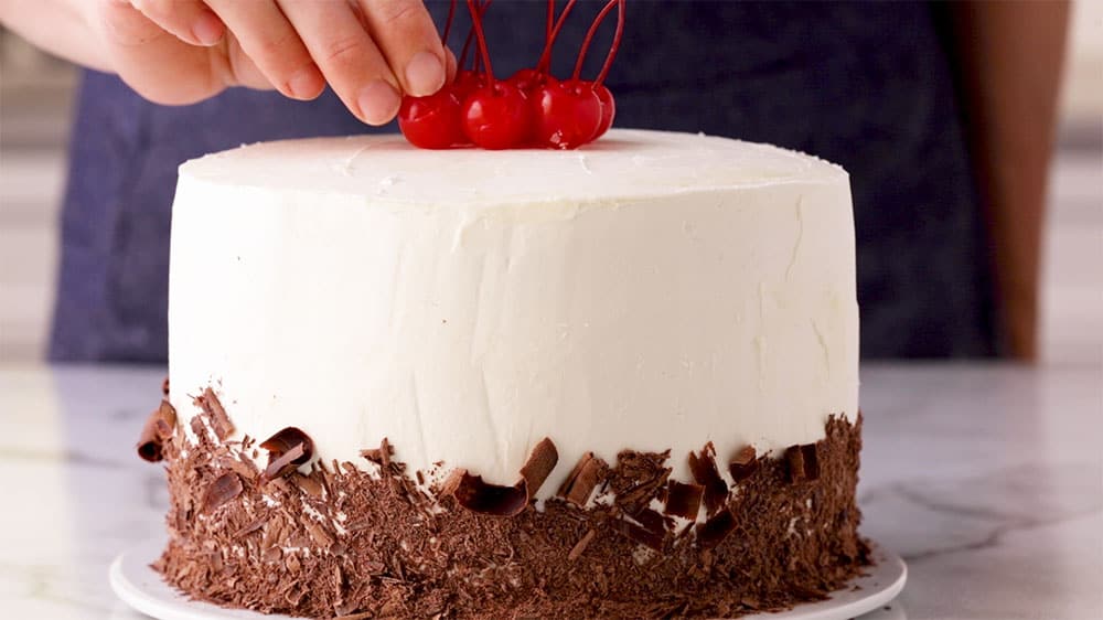 frosted cake with chocolate shavings and cherries on top