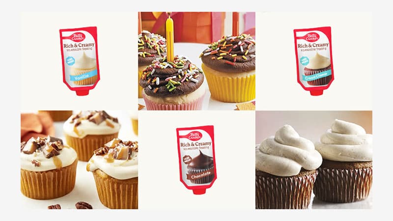 Assorted cupcakes with colorful toppings alongside Betty Crocker Rich & Creamy frosting pouches in vanilla, chocolate, and cream cheese.