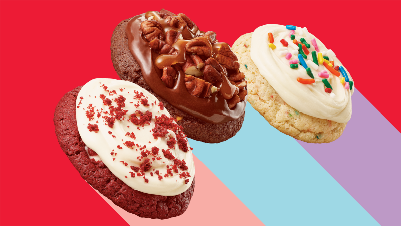 Three soft-baked cookies with frosting and toppings on a red background.