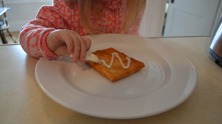 child putting frosting on a toaster strudel