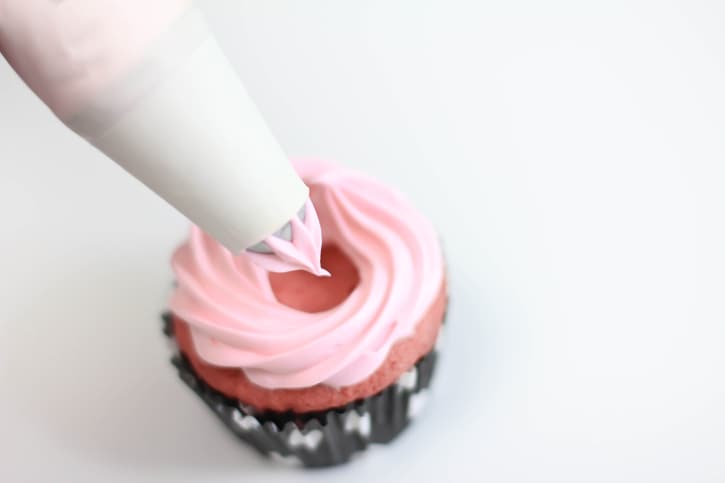 piping frosting onto top of baked cupcake