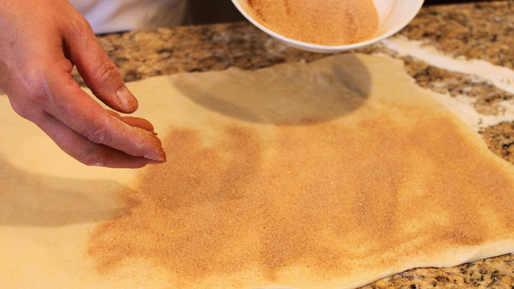 sprinkling dough sheet with cinnamon and sugar