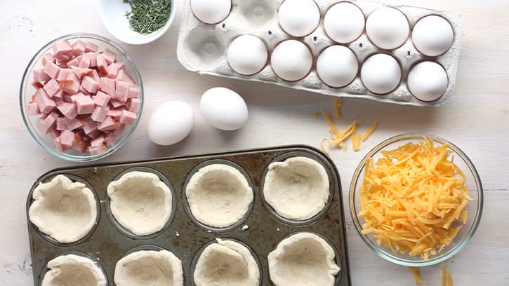 eggs, cheese, ham and cup dough in muffin baking sheet