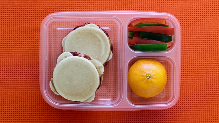 sliders in compartmented lunch container with orange and green and red pepper slices