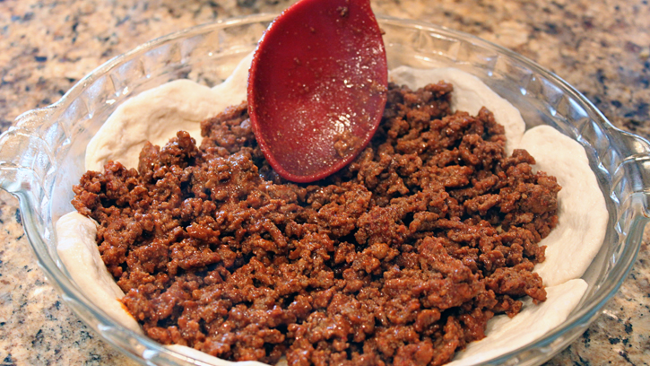 spreading cooked ground beef onto dough in pie plate